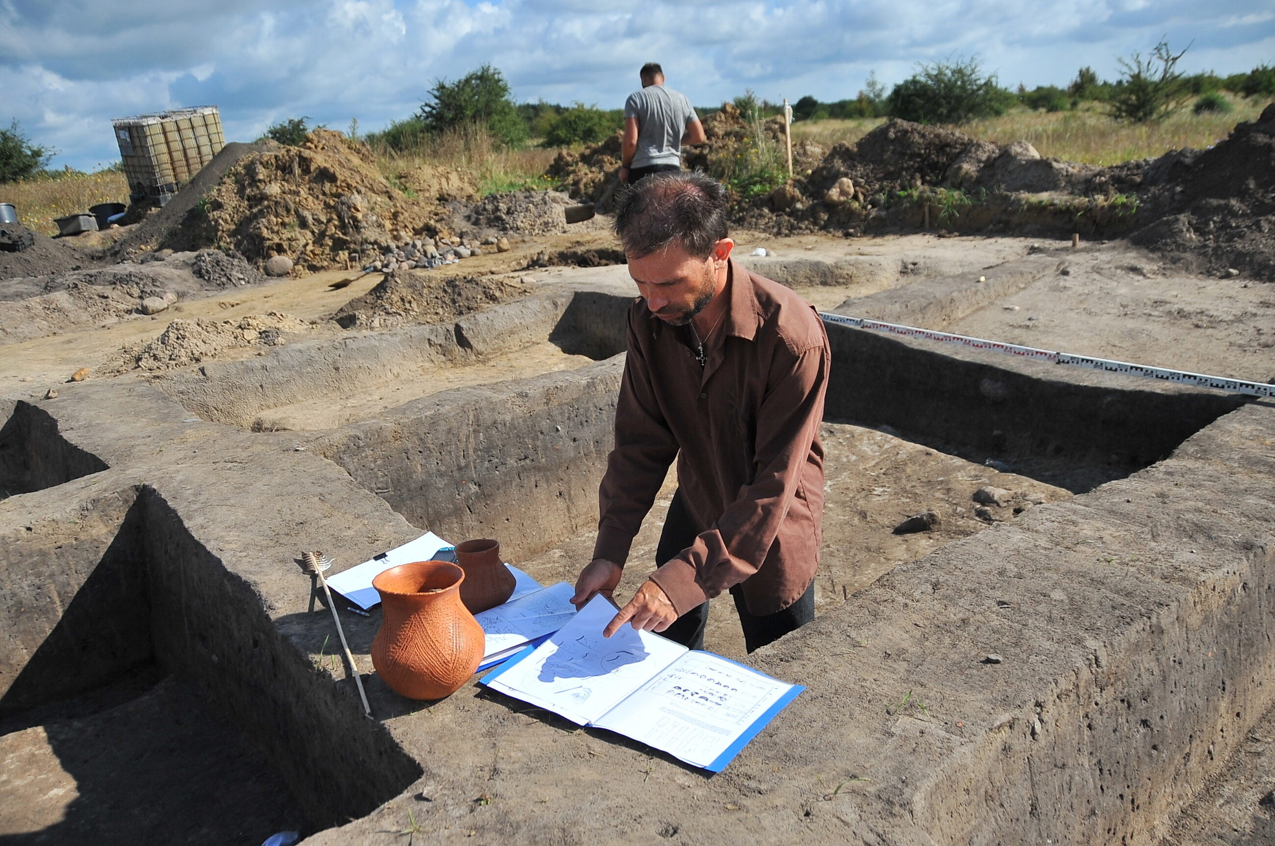 Prowadzący badania, archeolog Marcin Dziewanowski, pokazuje repliki glinianych garnków, podczas prac archeologicznych, w Stobnie.